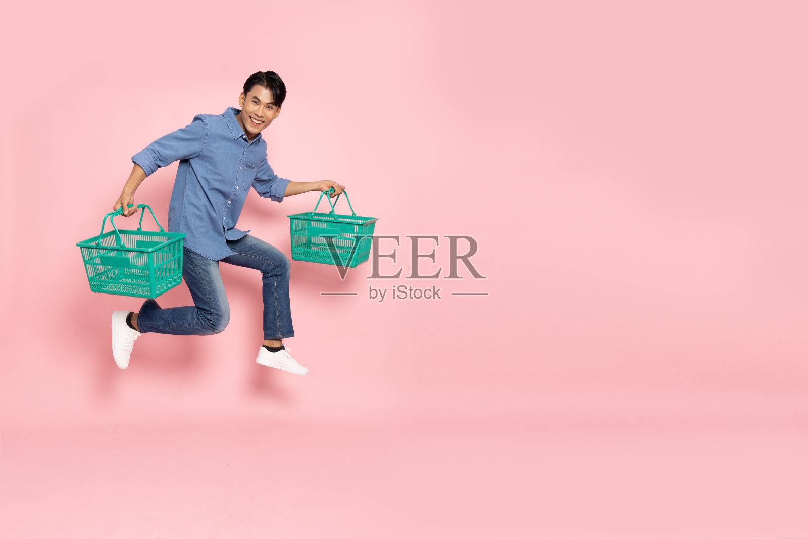 亚洲人跳,抱着绿色的杂货篮孤立在粉红色的背景,购物和超市的概念照片摄影图片
