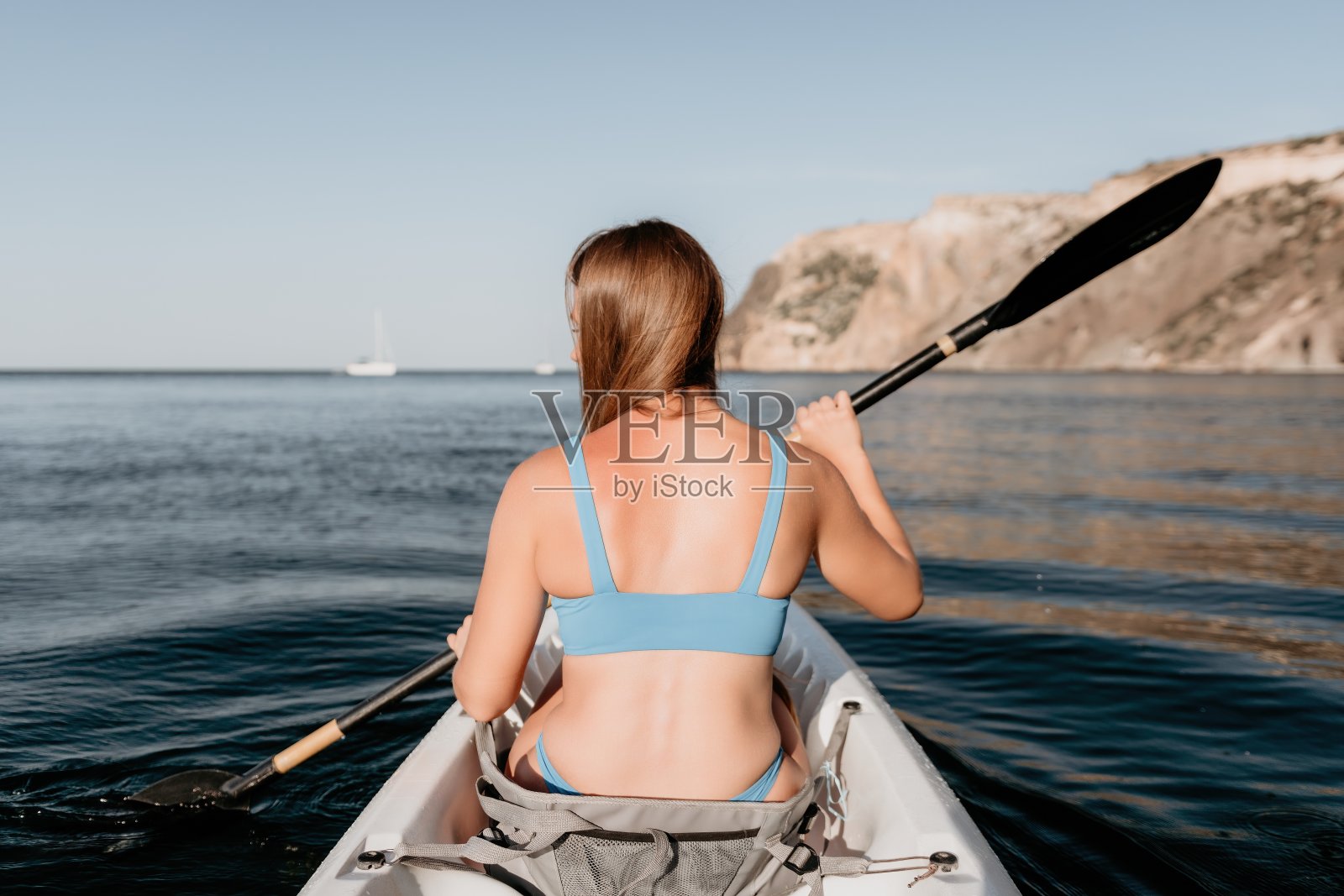 女子在皮艇后视图。快乐的年轻女子与长发漂浮在皮艇上平静的大海。暑假假期和开朗的女人们在船上放松玩乐。照片摄影图片