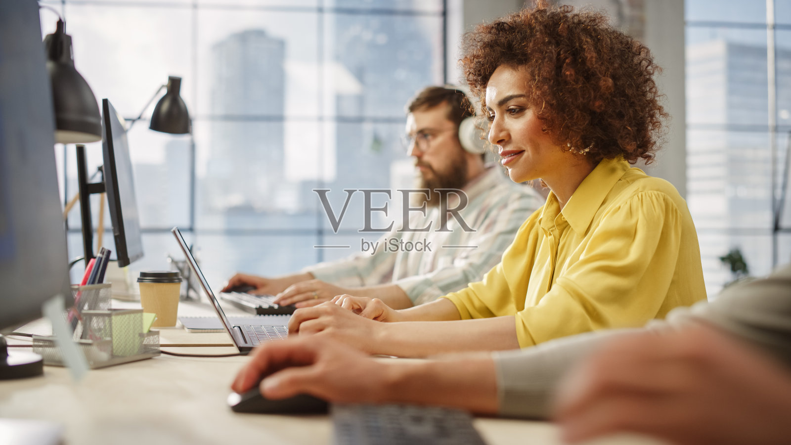 在明亮的当代办公室里,年轻女子微笑着使用笔记本电脑。客户顾问回复客户支持邮件。团队合作,在框架内解决问题照片摄影图片