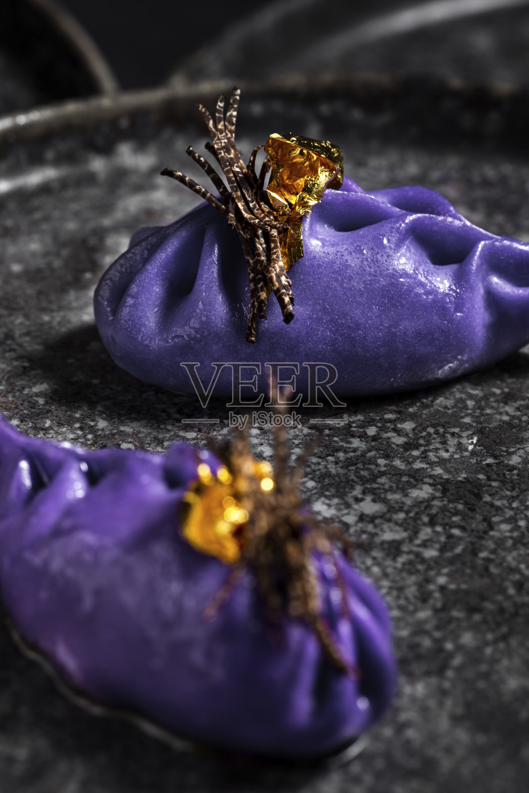 黑色盘子里放着带松露条纹和金箔的紫色饺子照片摄影图片