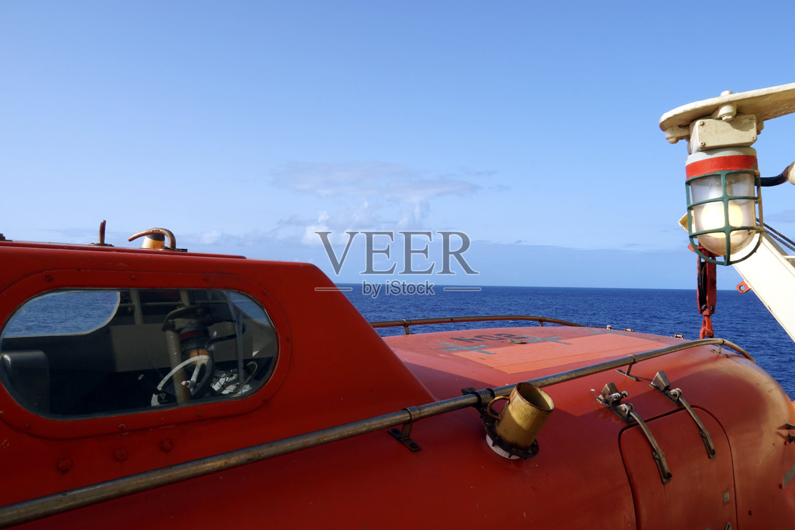 近距离观察橙色救生艇的船舱,反光胶带贴用吊柱和安全钩固定。照片摄影图片