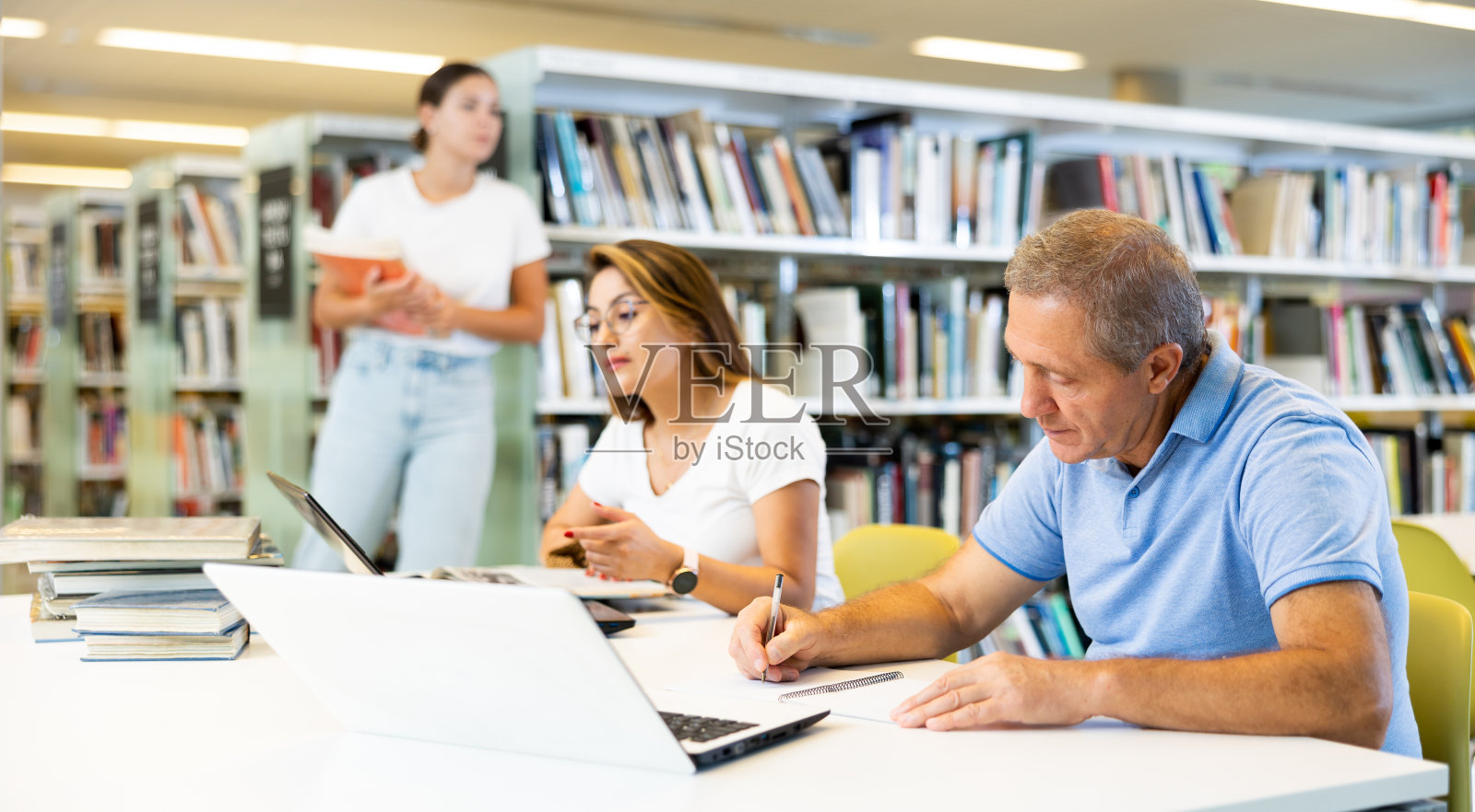 成熟的男人花时间在图书馆,看书和做笔记本电脑。自我教育的概念照片摄影图片