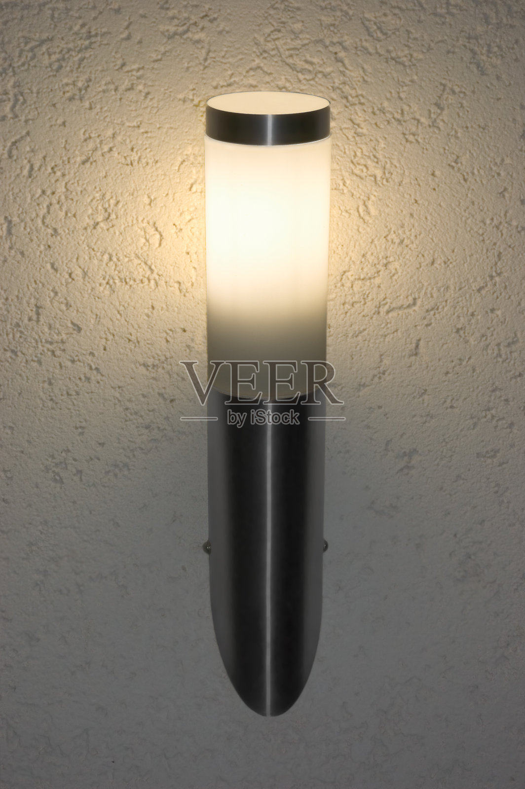 夜间明亮发光的不锈钢户外壁灯,大型垂直壁灯特写,浅灰色纹理灰泥图案背景阴影,细节纹理照片摄影图片