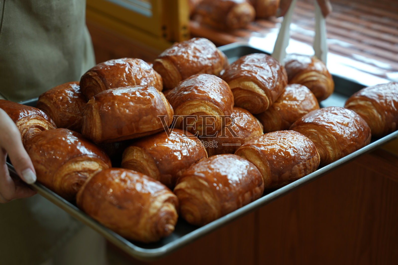 一个年轻的面包店老板在他的店里拿着一盘刚烤好的巧克力羊角面包。照片摄影图片