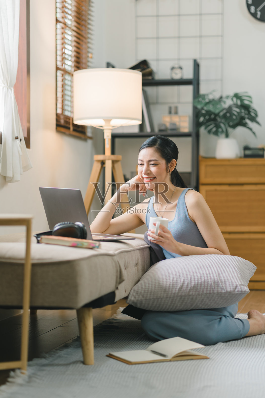 千禧一代的亚洲女孩坐在客厅的沙发上,用笔记本电脑做笔记学习。这位专注的年轻女子在电脑上工作,在笔记本上写字,在家里参加在线课程或培训。照片摄影图片