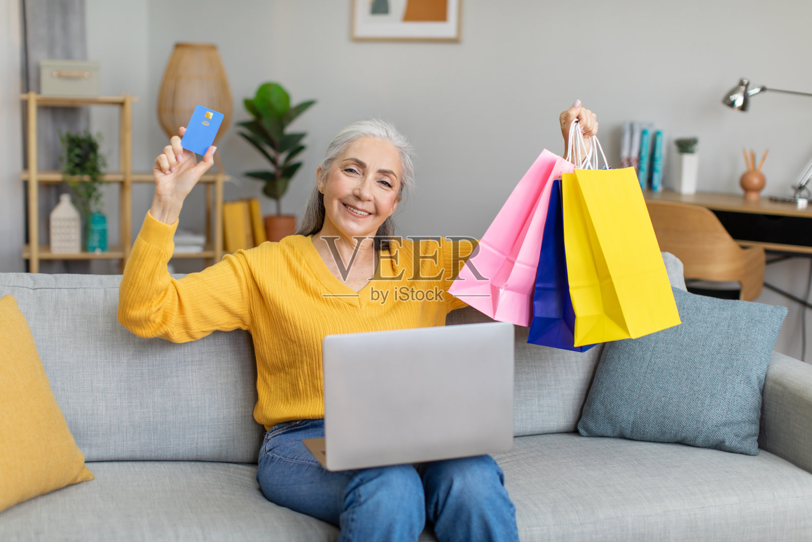 开朗的白人老太太坐在沙发上,拿着笔记本电脑,给我看了很多包裹,里面装着购物用品和信用卡照片摄影图片