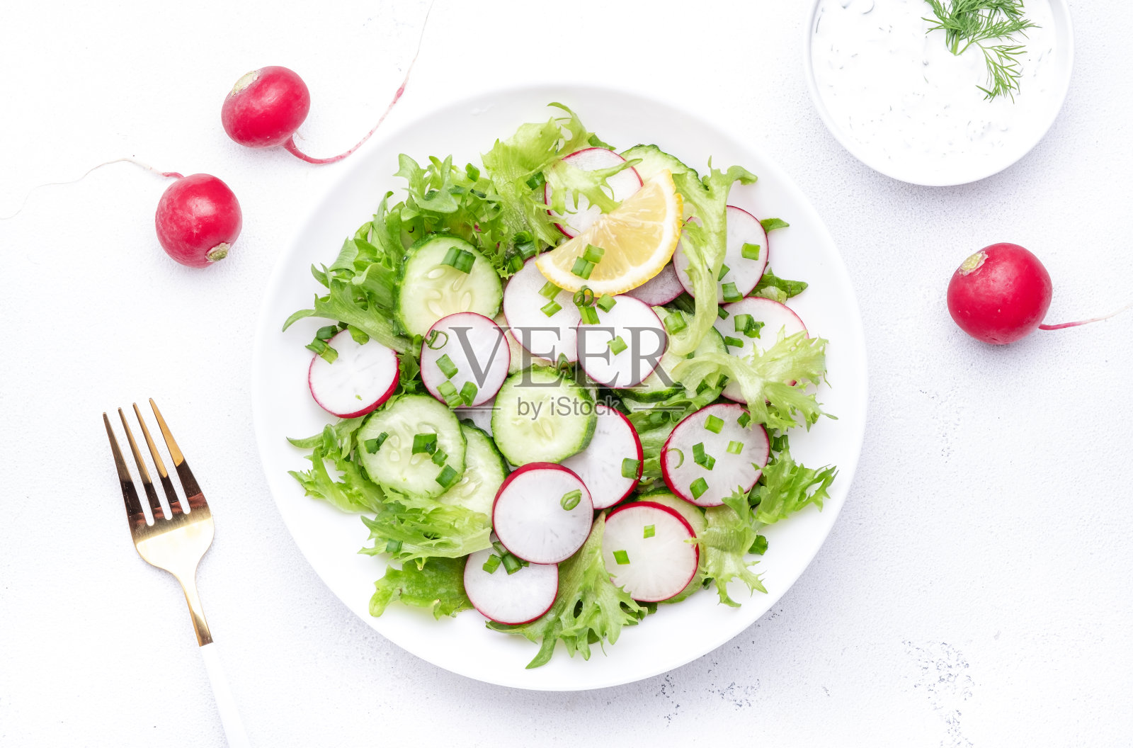 新鲜的夏季沙拉,配以萝卜、黄瓜、生菜和葱,配以希腊酸奶酱,白色桌面背景,俯视图照片摄影图片