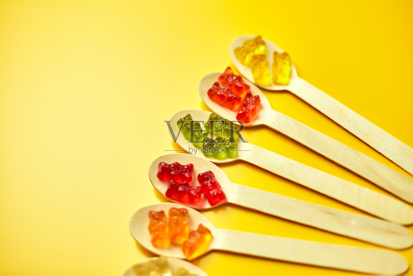平铺构图与美味的果冻熊糖果在木勺,软糖熊在黄色背景,俯视图,复制空间。照片摄影图片