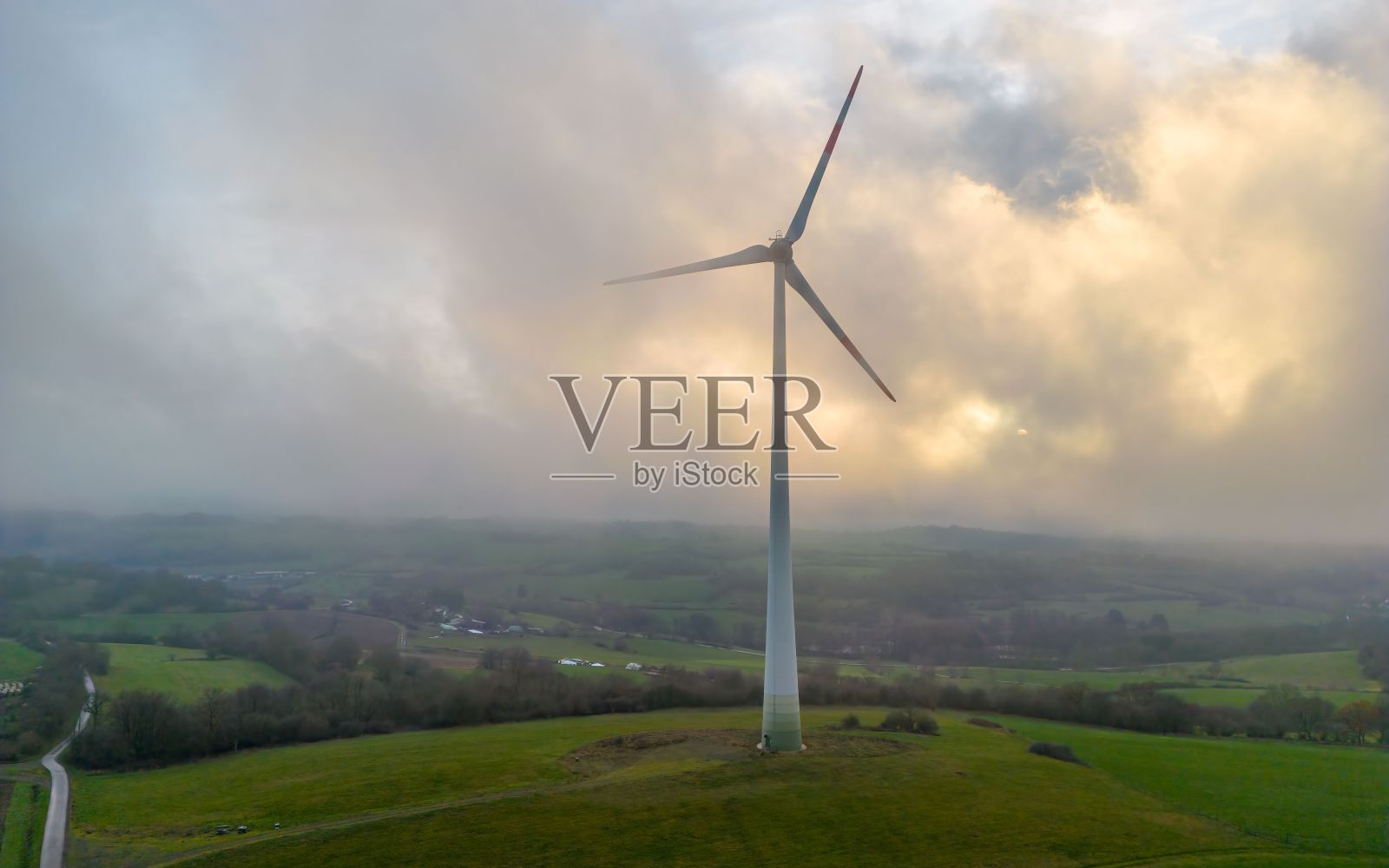雄伟的风车矗立在多云的天空中,周围是郁郁葱葱的绿色田野照片摄影图片