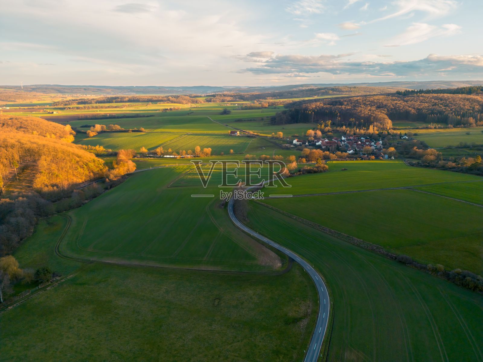 在黄金时段,无人机拍摄的一条被绿色植物包围的乡村道路照片摄影图片