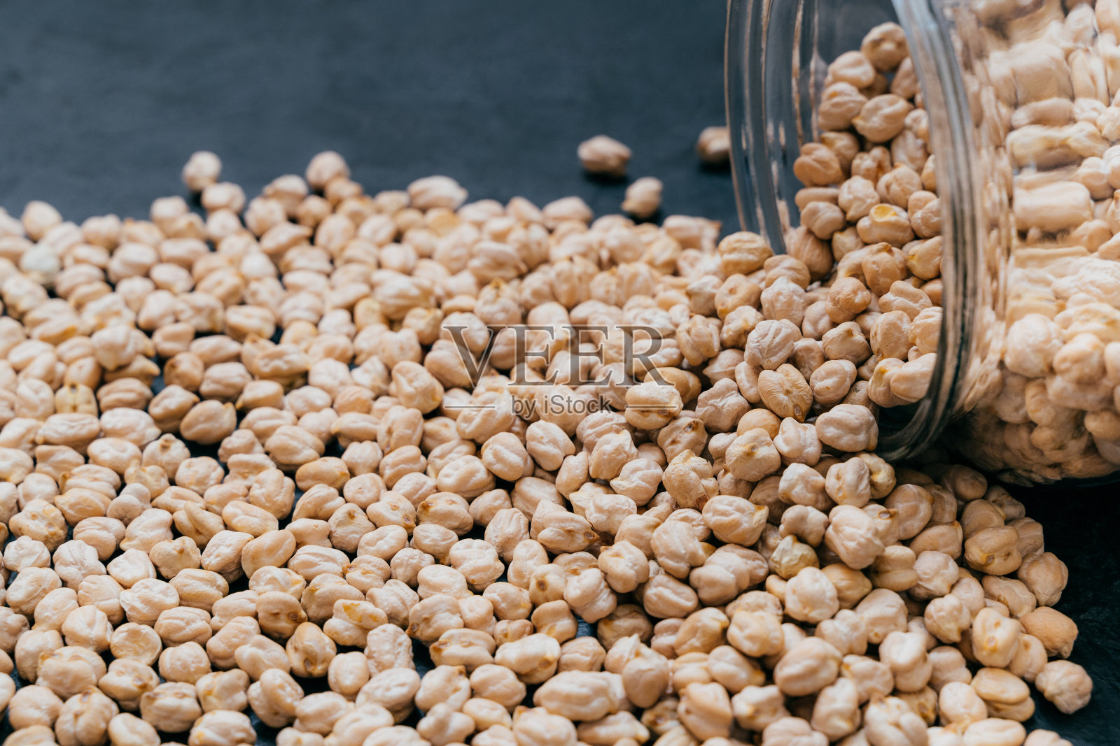 装有生鹰嘴豆的玻璃罐。在暗背景上分离的鹰嘴豆粒。特写镜头。蛋白质的种子。健康食品。素食成分照片摄影图片