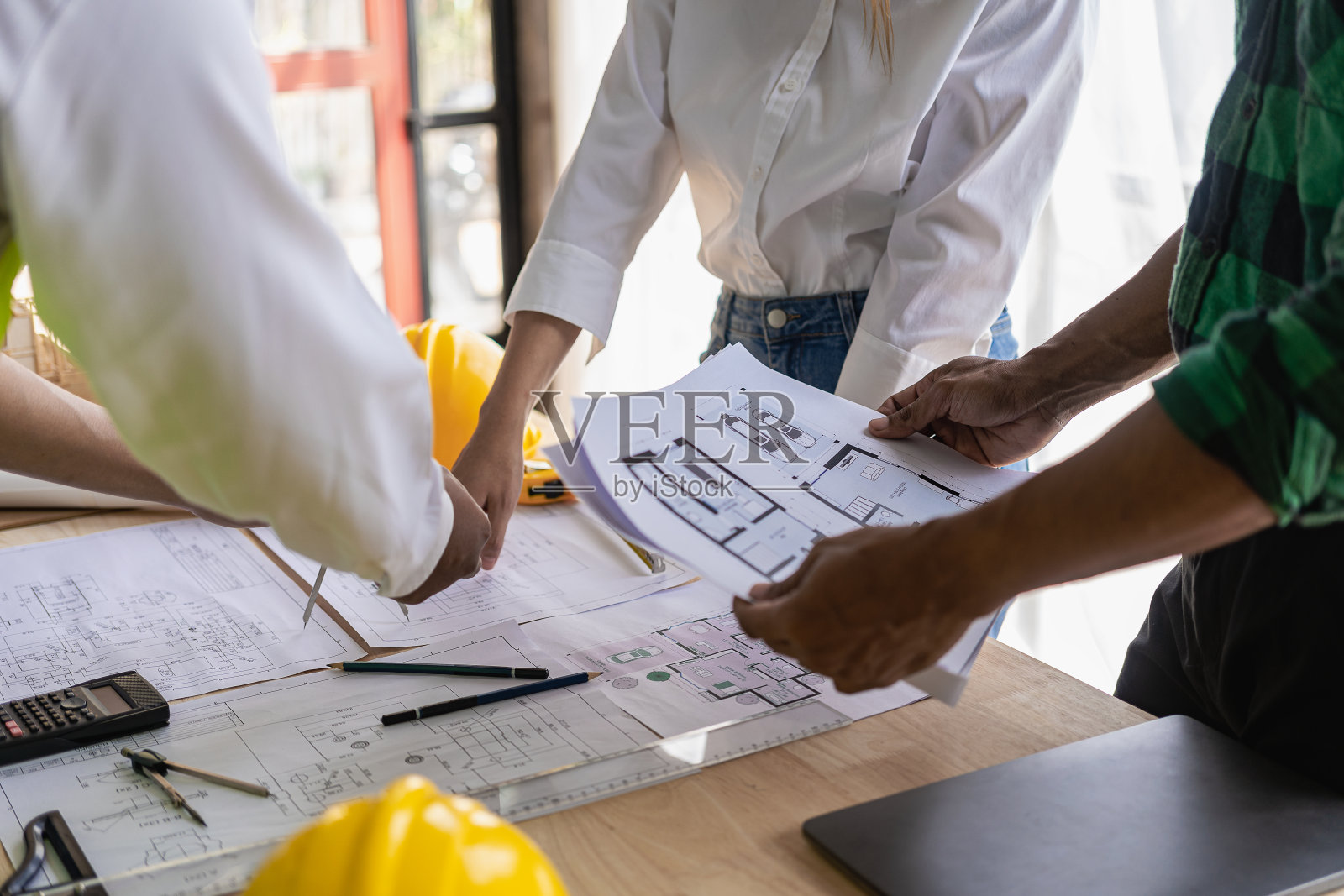 工程师指向蓝图并使用笔记本电脑绘制项目设计建筑,建筑承包商和工头与楼层平面图会面,用于房地产开发项目行业照片摄影图片