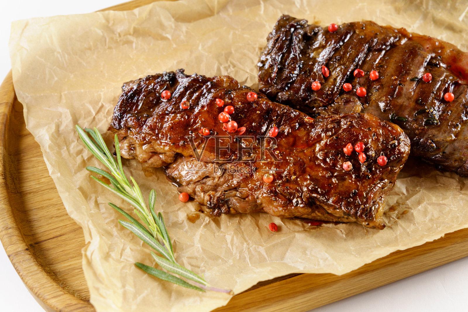 木板上的烤牛排,近距离,迷迭香。照片摄影图片