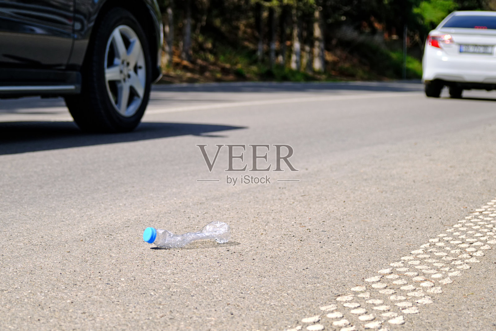 一个空的塑料水瓶被扔在乡间小路上,背景是一辆过往的汽车。照片摄影图片