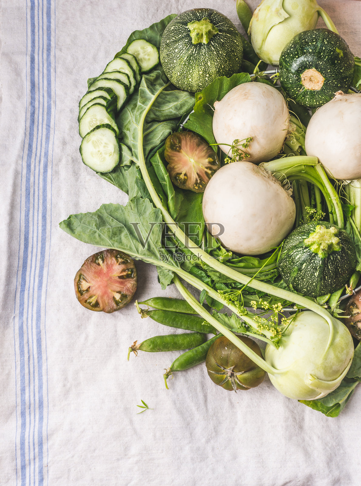 各种绿色蔬菜堆在浅色的桌子上:青豆、甘蓝、生菜、西葫芦、黄瓜、绿番茄。前视图。照片摄影图片