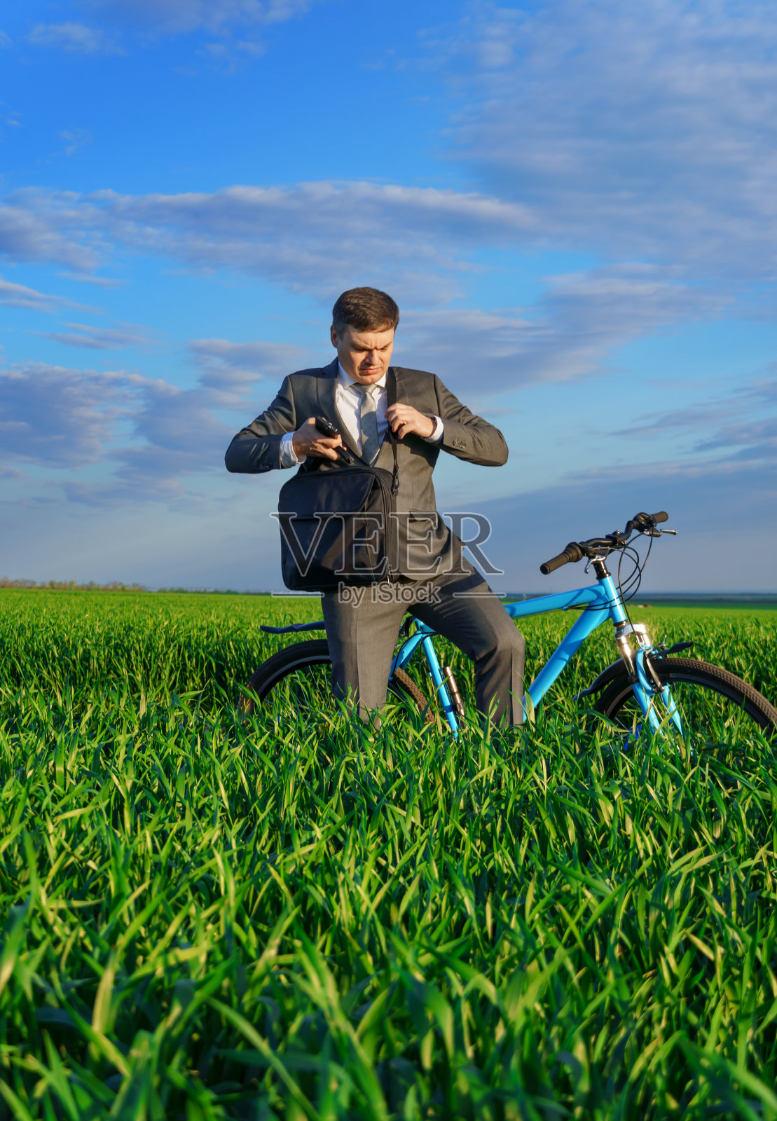 一位商人骑着自行车在绿油油的草地上,穿着商务套装,春日里美丽的大自然,自由职业者的经营理念照片摄影图片
