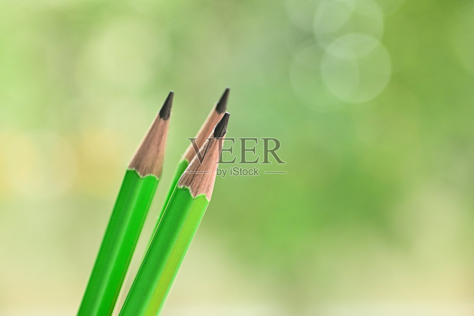 三尖的绿色木制铅笔在模糊的自然背景与散景照片摄影图片