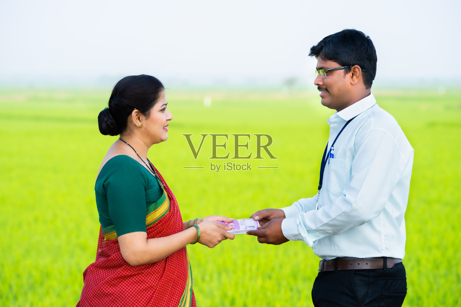 快乐微笑的印度妇女在稻田从银行家那里拿钱——财政支持、就业和农业综合企业的概念照片摄影图片