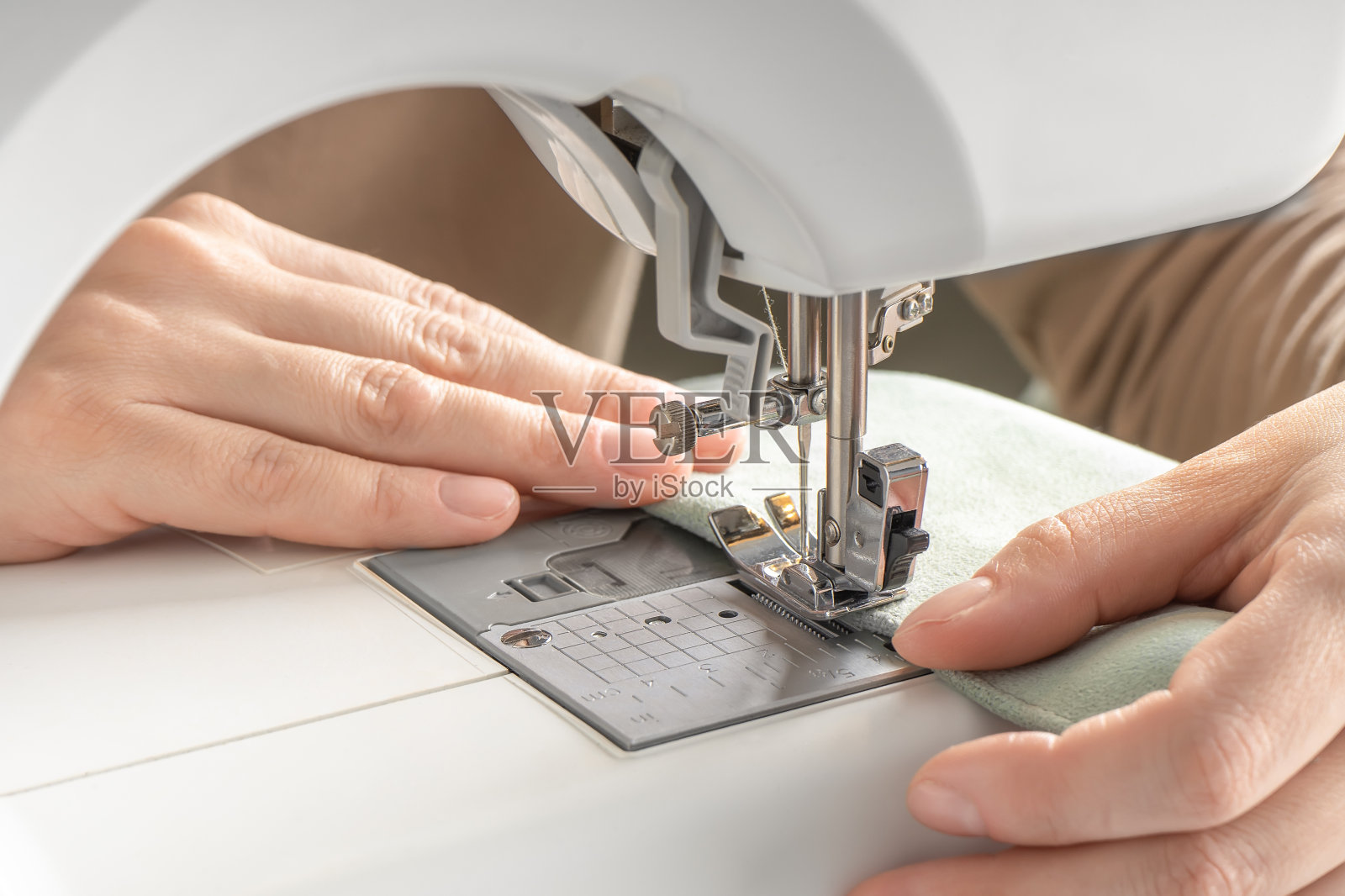 女工的双手在工作室的现代缝纫机上缝制白色布料照片摄影图片