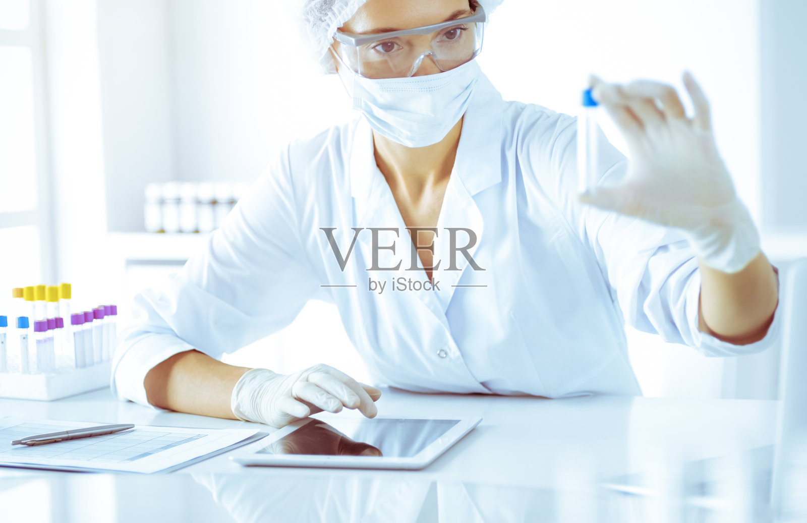 专业的女科学家戴着防护眼镜,在阳光明媚的蓝色实验室里拿着试剂进行研究。医学和科学研究照片摄影图片