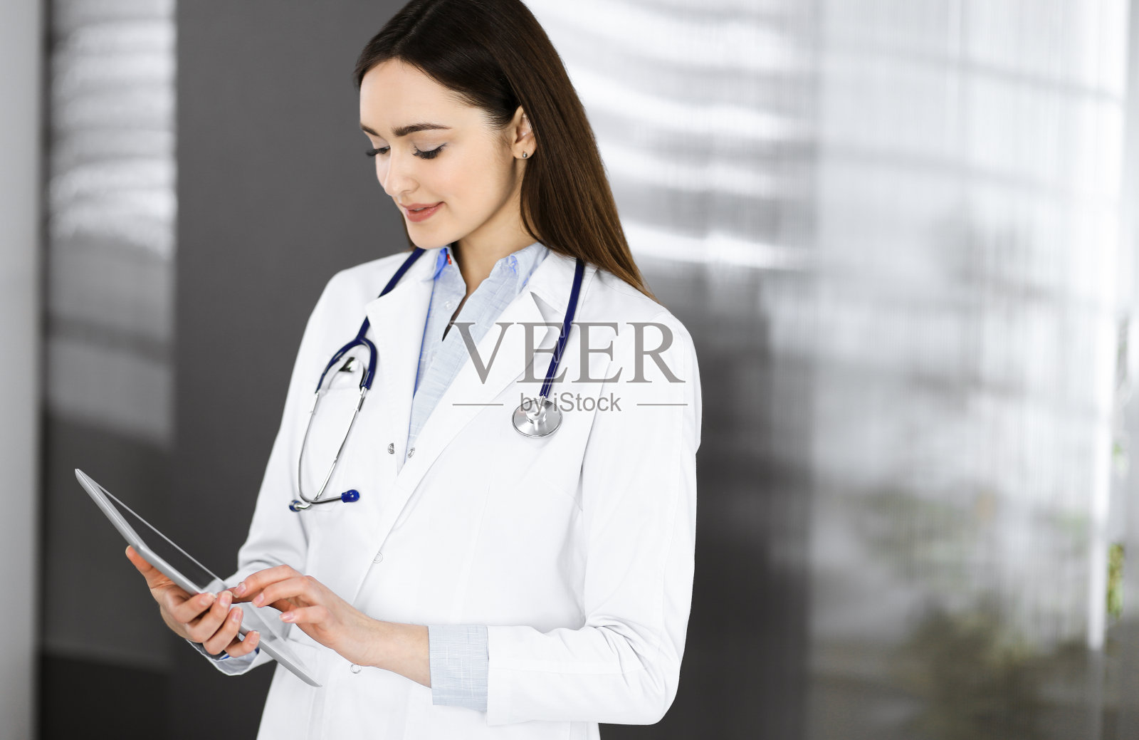 开朗聪明的女医生站在诊所里,手里拿着一台平板电脑。一个友善的女医生的肖像。医院里完美的医疗服务。医学的概念照片摄影图片