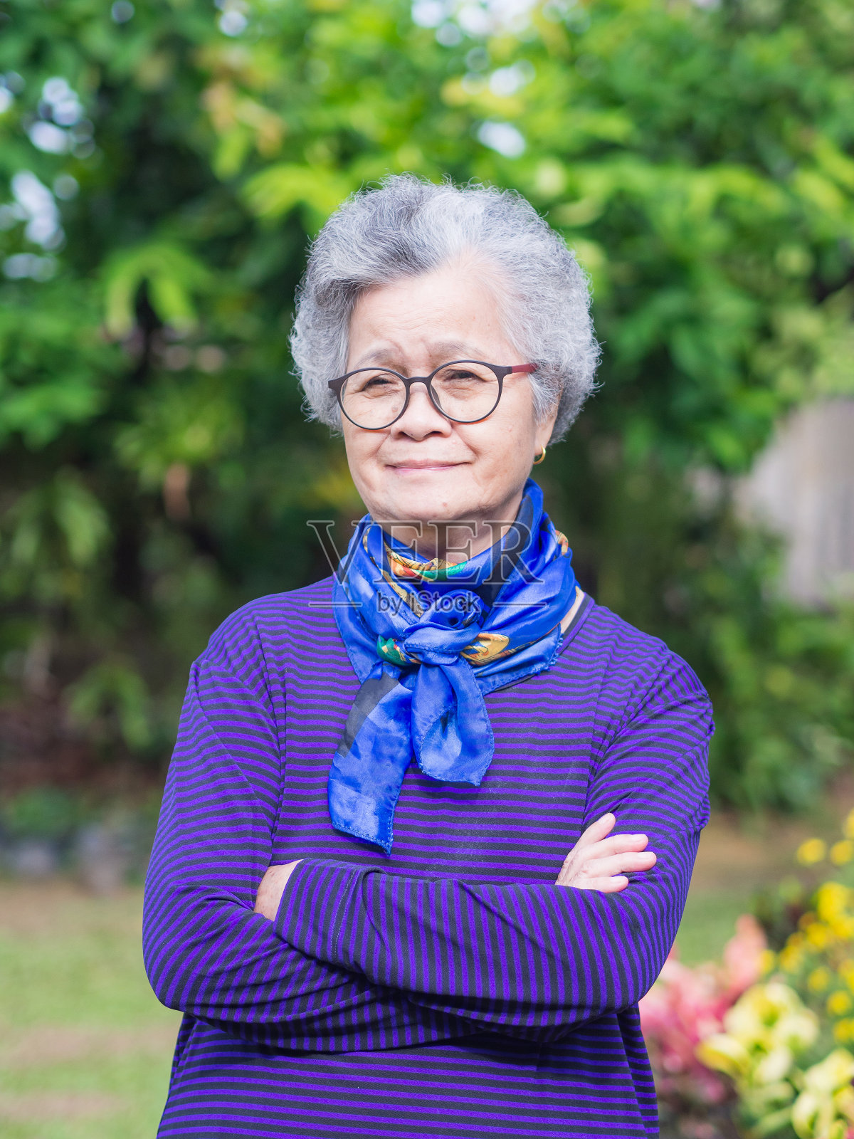 一位灰白短发的老年妇女的肖像,双臂交叉,站在花园里微笑着看着镜头。照片摄影图片