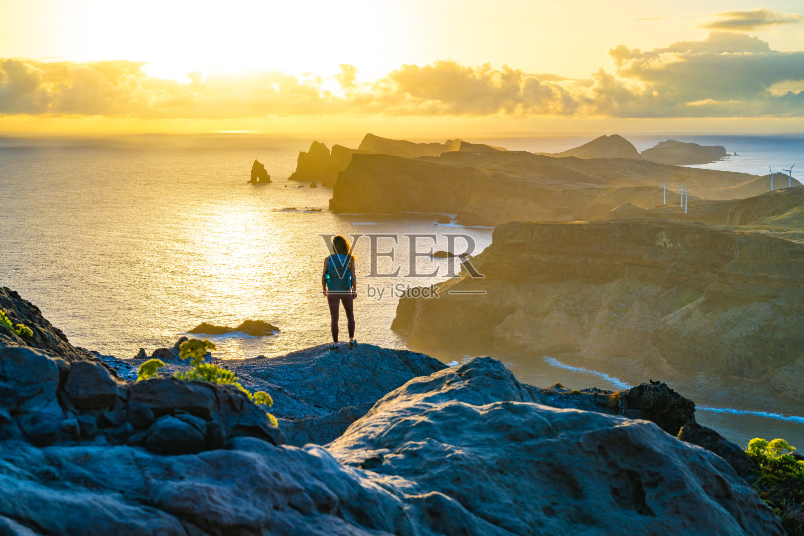 背包客游客在日出时在陡峭的悬崖上欣赏海景,沿着马德拉海岸崎岖的山麓欣赏全景。Ponta do Bode,马德拉岛,葡萄牙,欧洲。照片摄影图片