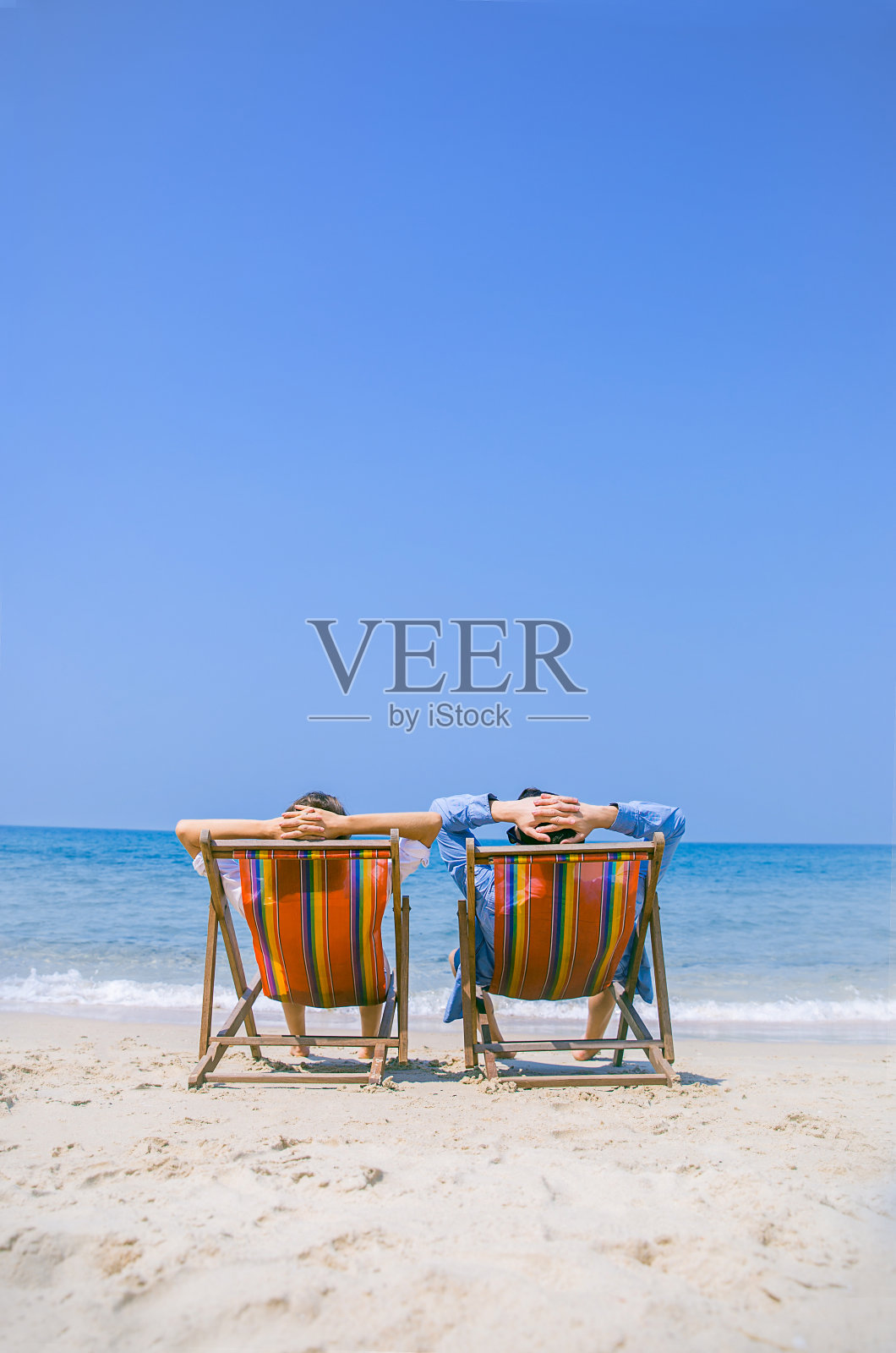 一对快乐的退休夫妇在海滩上欣赏美丽的日落。一对夫妇在热带岛屿的海滩上放松,享受美丽的大海。夏季海滩度假概念照片摄影图片