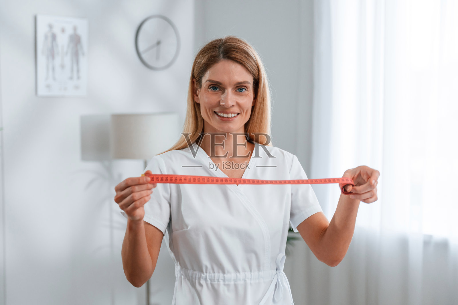 手里拿着卷尺,饮食的概念。穿白大褂的年轻女医生在室内照片摄影图片