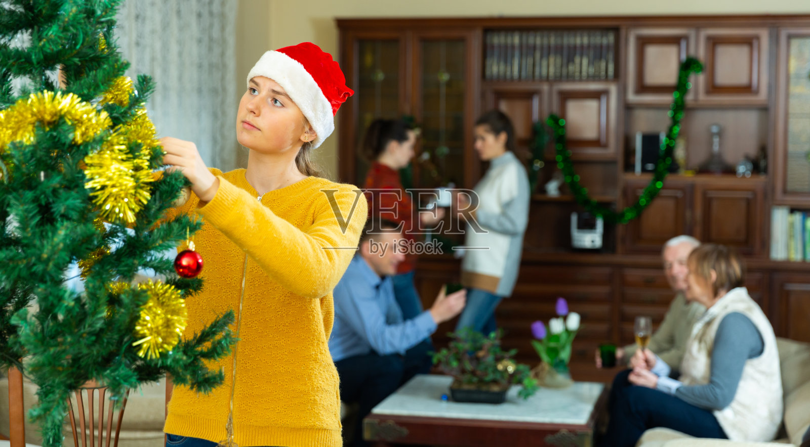 十几岁的女孩装饰圣诞树。大家庭在房间里聊天照片摄影图片