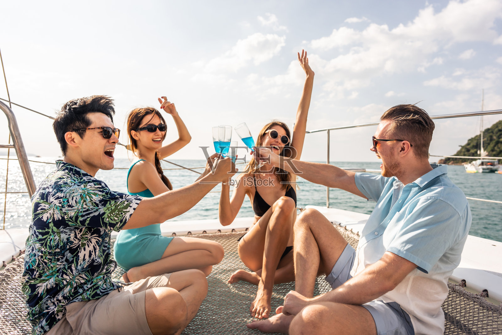 一群不同的朋友在游艇上开派对,喝着香槟。迷人的年轻男女聚在一起,庆祝节日,双体船在夏日夕阳下航行。照片摄影图片