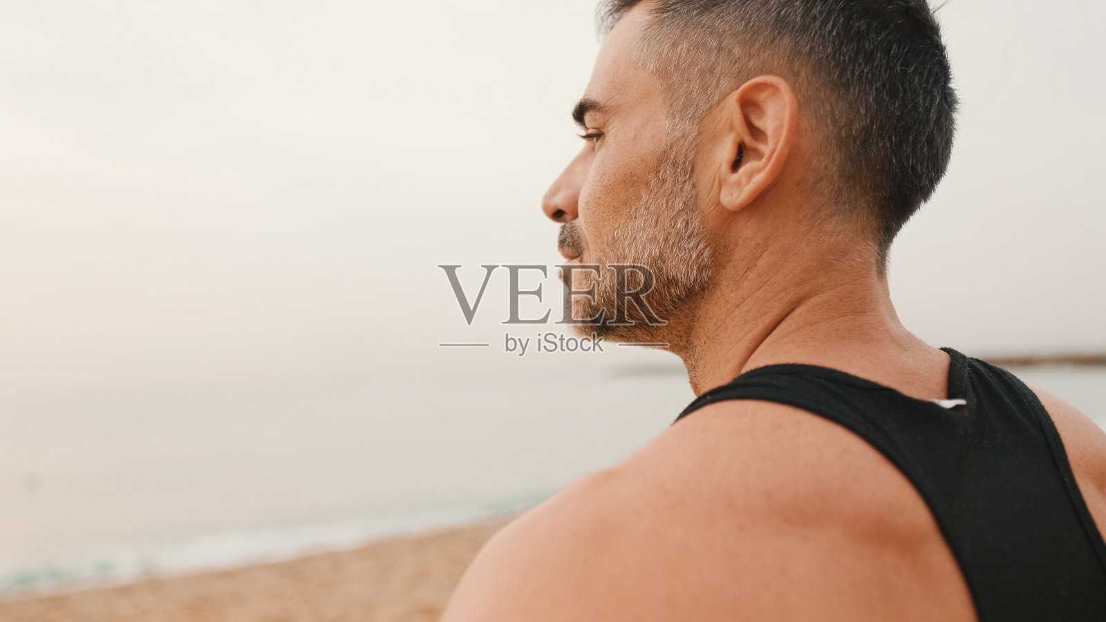 中年运动员运动后站在沙滩上看海景的特写照片摄影图片