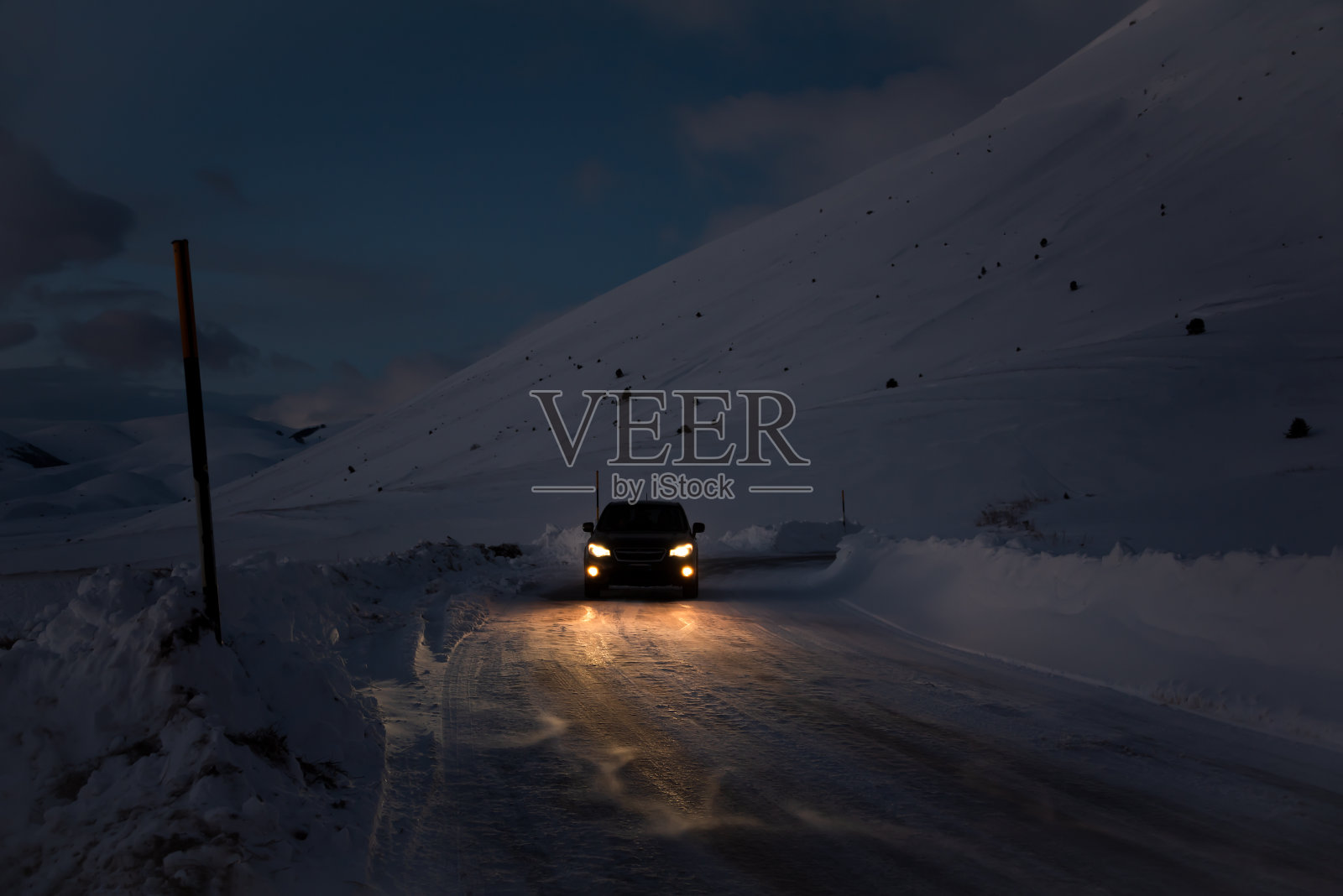 汽车行驶在黑暗的冬季道路上,周围是积雪覆盖的山脉照片摄影图片