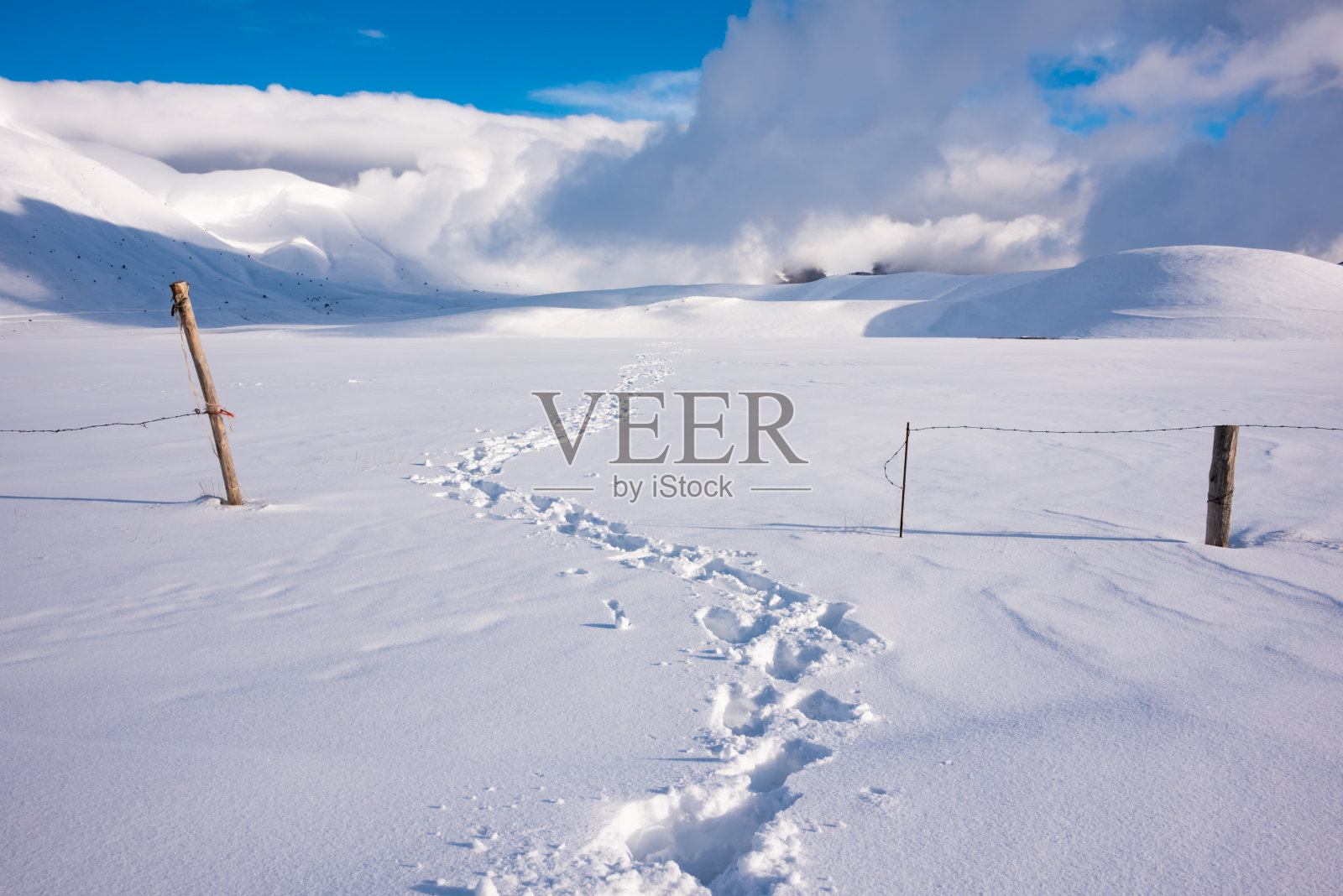 冬日的风景,在阳光明媚的日子里,雪谷上的足迹小径和栅栏照片摄影图片