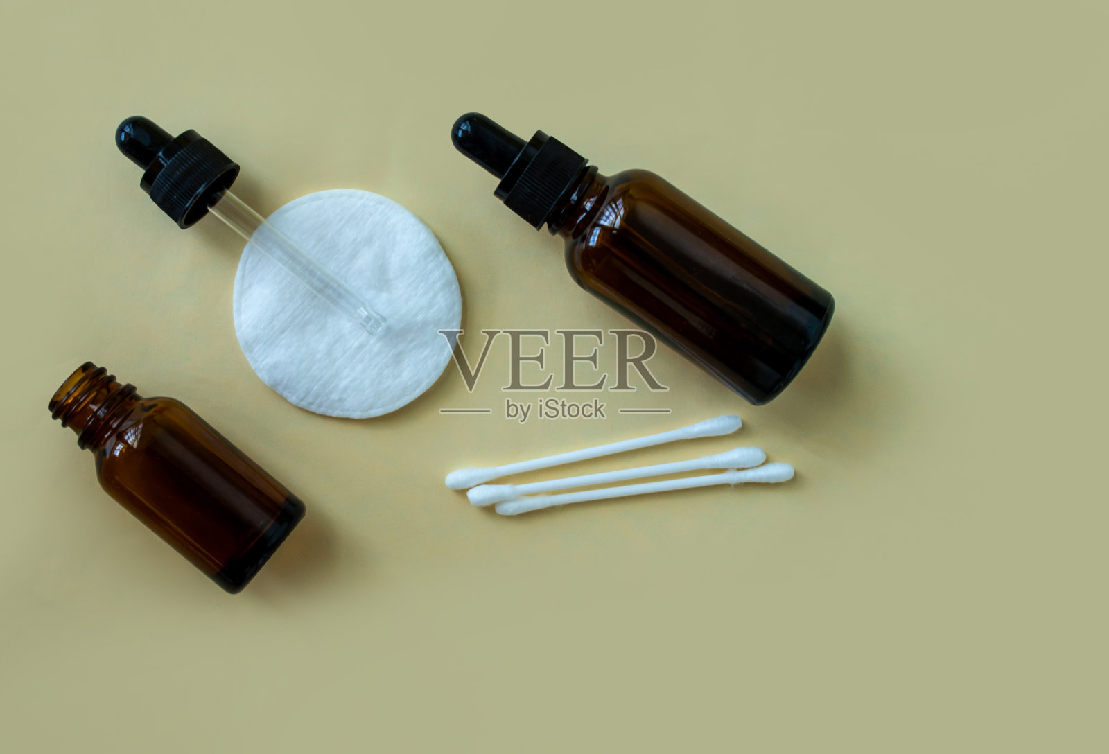 平放着装有化妆品移液管和棉垫的瓶子,米色背景上有棉签。照片摄影图片