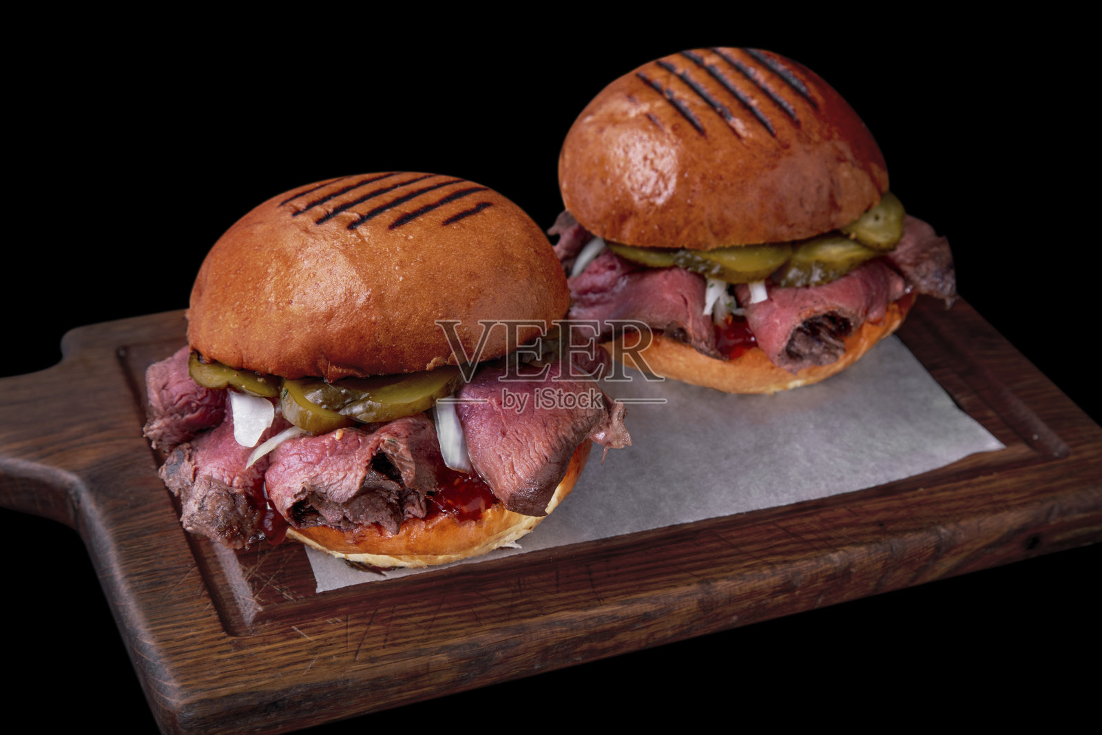 黑色背景的木板上放着两个汉堡和炸猪排、腌黄瓜、洋葱番茄酱和酱汁照片摄影图片