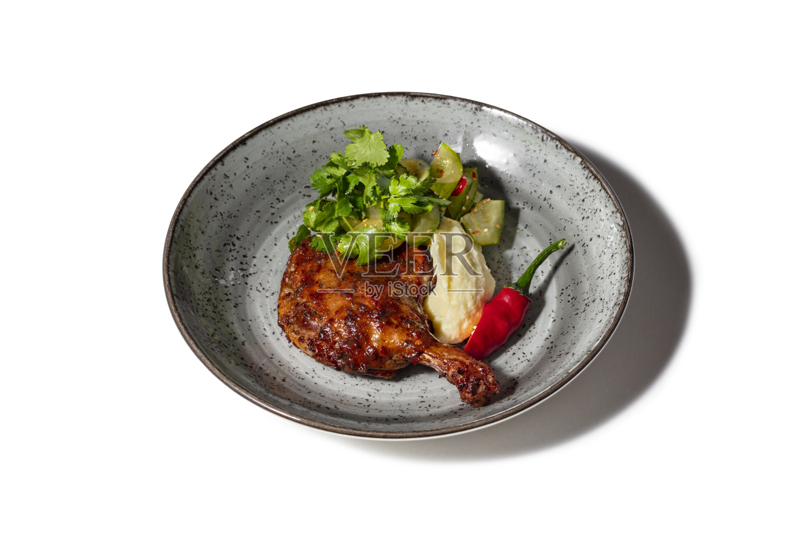 樱桃酱烤鸭腿配土豆泥和黄瓜沙拉,辣椒配糖醋酱撒芝麻。旁边放着香菜叶和半个辣椒。食物放在一个圆形的陶瓷盘子里。白色背景。照片摄影图片