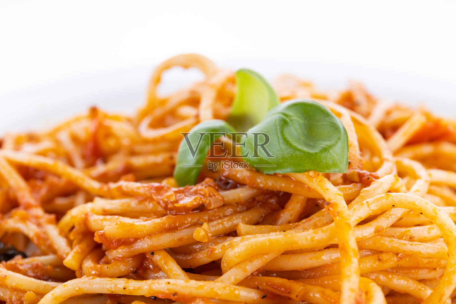 白色盘子里的意大利面,白色背景上的罗勒叶。照片摄影图片