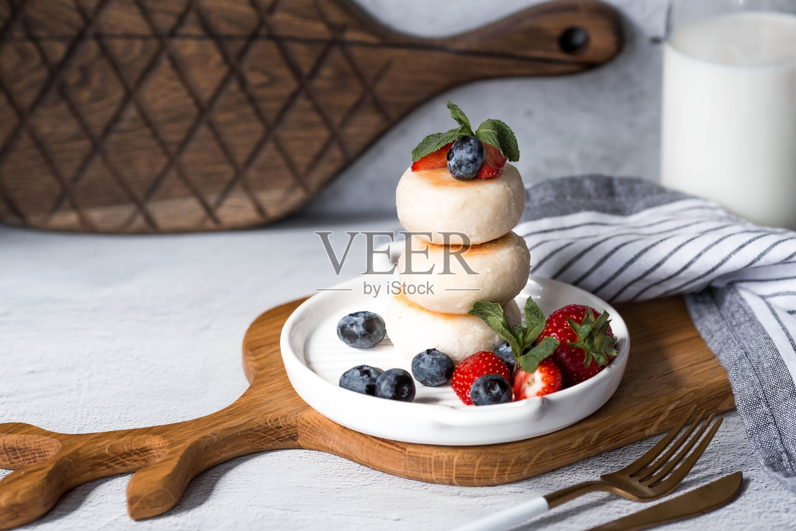 灰色混凝土桌子上时髦的木板上放着松软干酪煎饼、俄罗斯奶酪蛋糕和新鲜的蓝莓、草莓和薄荷。自然产品。健康美味的早餐。照片摄影图片