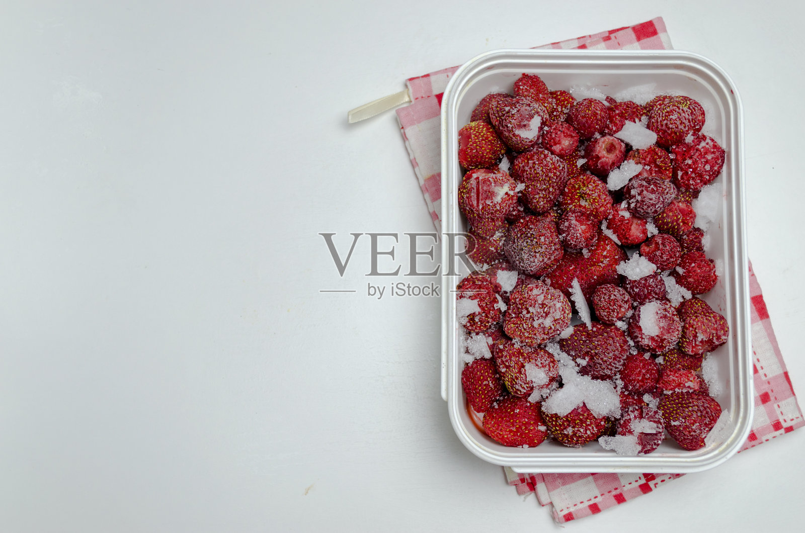 白色背景的塑料容器里的冷冻草莓。照片摄影图片
