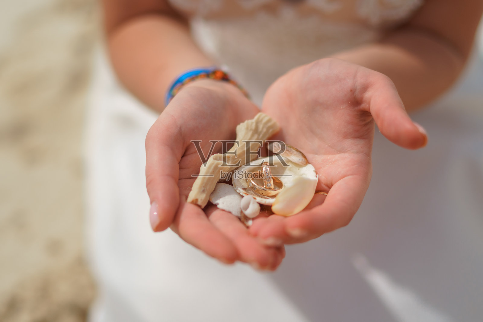 一个女孩手里的结婚戒指和小贝壳。照片摄影图片