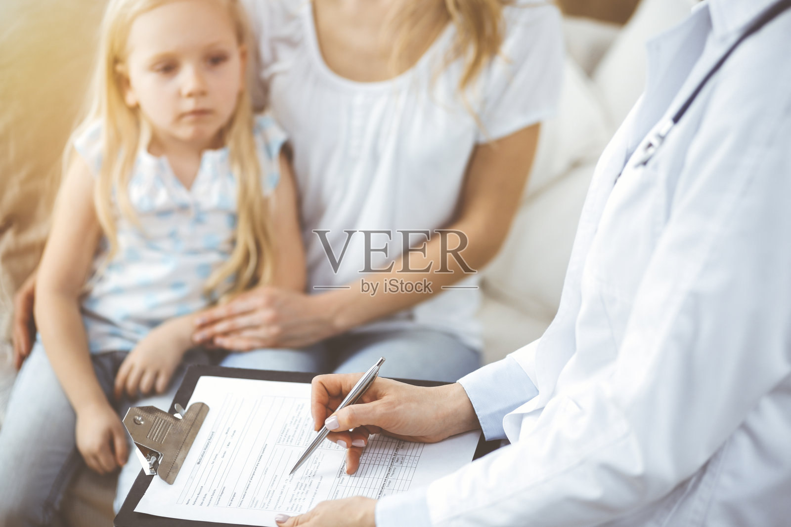 医生和病人。儿科医生在家里给小女孩和她妈妈做检查时使用了剪贴板。生病和不高兴的孩子在体检照片摄影图片
