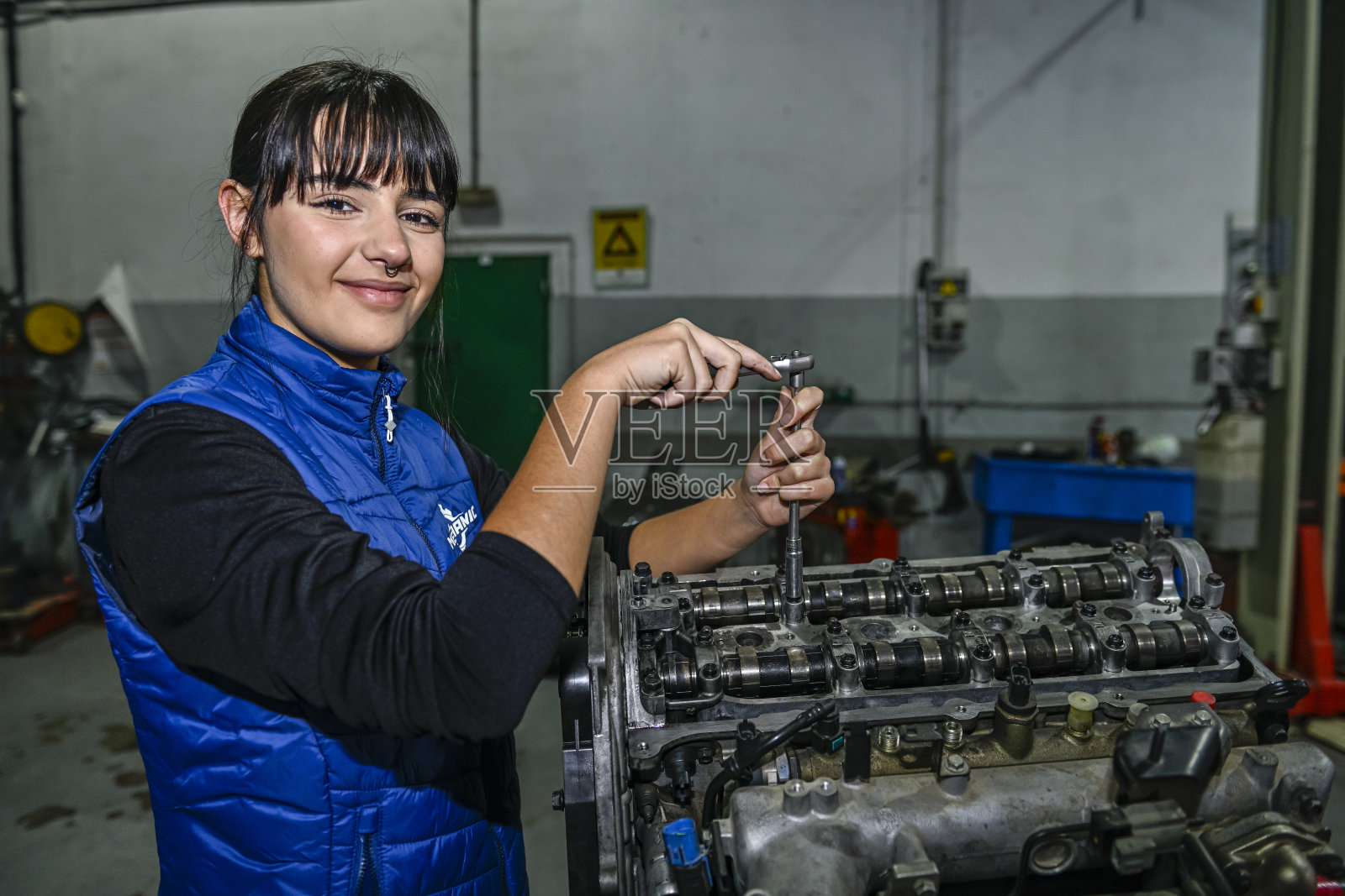 年轻的女机械师,正在修理汽车发动机。照片摄影图片