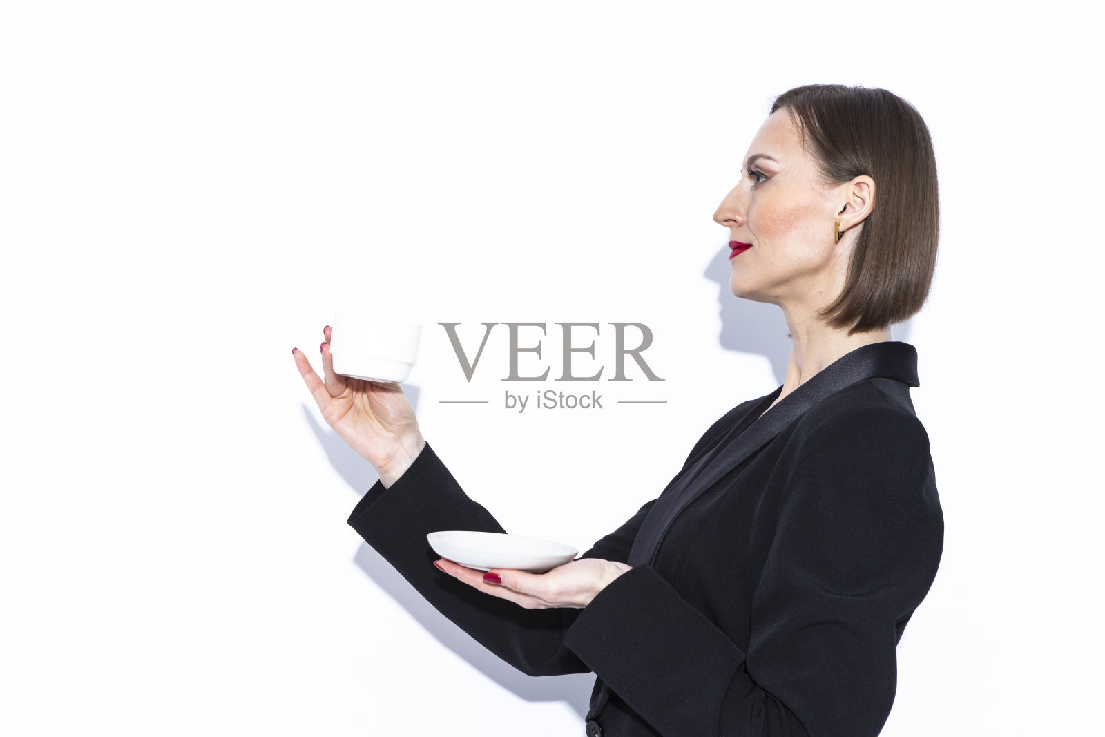 迷人的肖像,积极自信的白人商务女性在黑色西装摆姿势与咖啡茶杯在白色背景。照片摄影图片