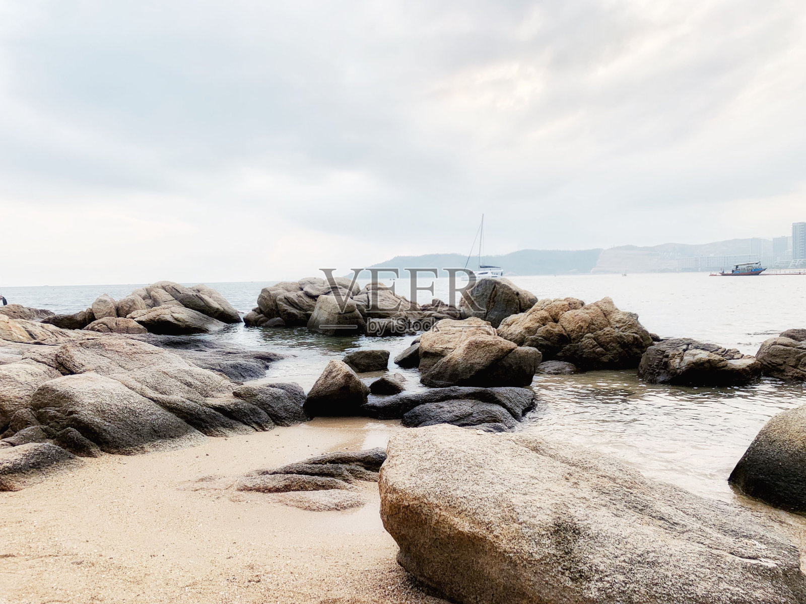 落潮时,岩石嶙峋的海岸线,背景中有两艘船照片摄影图片
