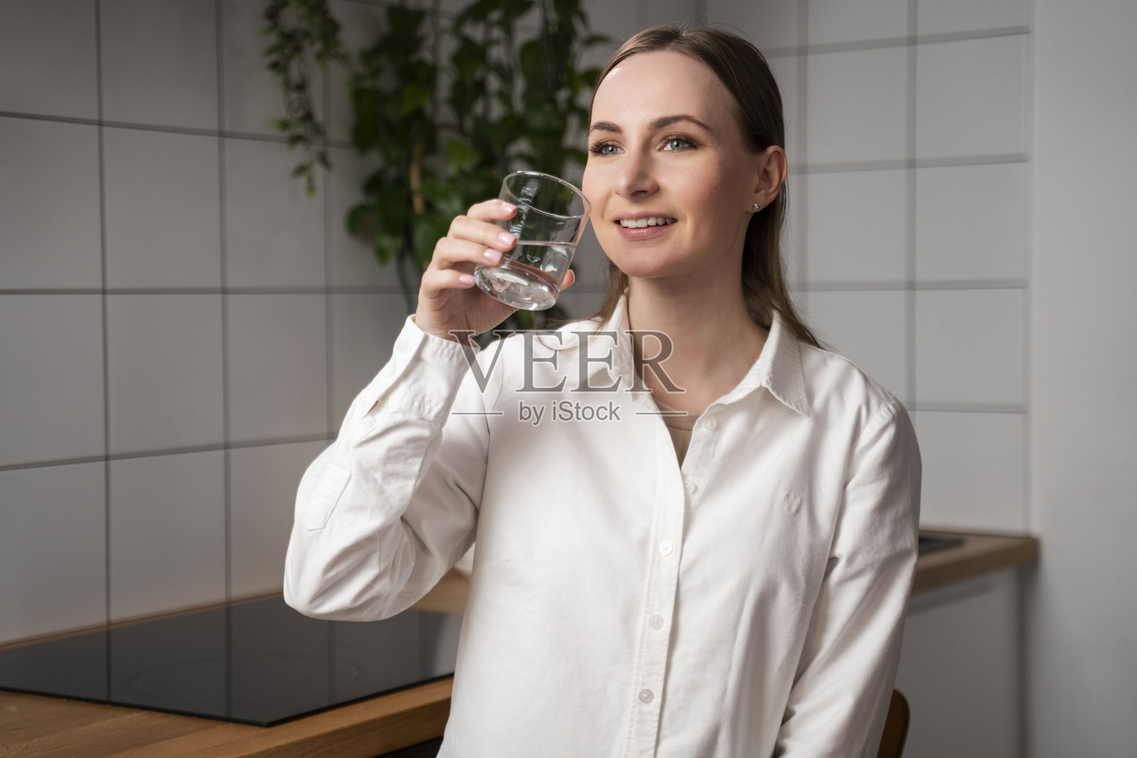年轻女子喜欢站在厨房里用玻璃杯喝干净的过滤水。健康的生活方式照片摄影图片