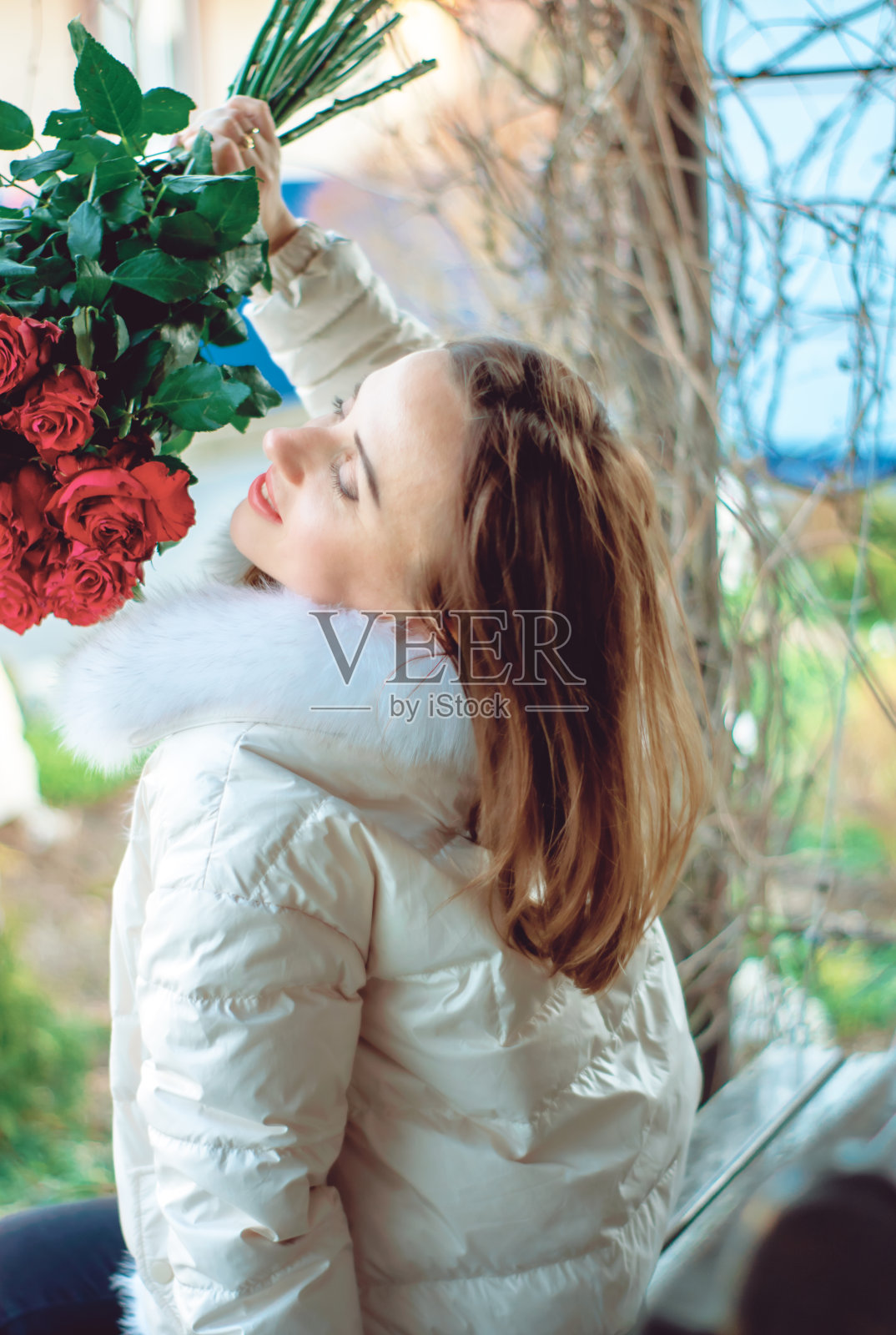 一个美丽的女人坐在长凳上享受玫瑰的香味。照片摄影图片