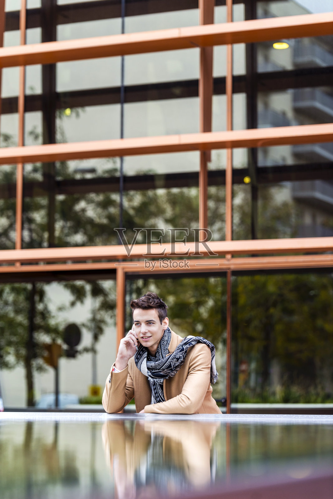 时尚帅气的年轻人穿着外套站在户外,靠在墙上使用智能手机照片摄影图片