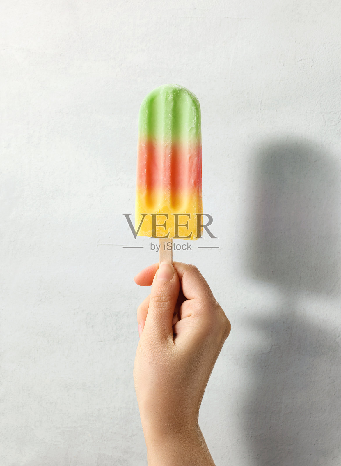 在浅灰色的背景上,女人手里拿着五颜六色的水果冰棒照片摄影图片
