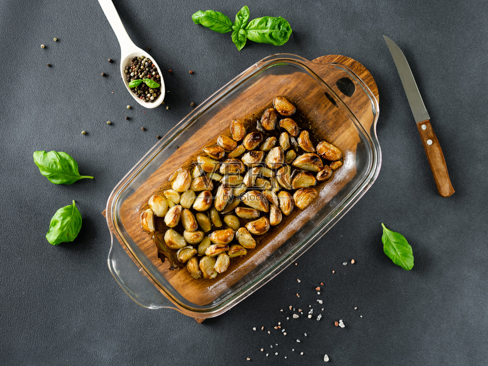 蒜头与橄榄油和香料一起烘烤。烤大蒜,黑胡椒和罗勒放在木板上。俯视图照片摄影图片